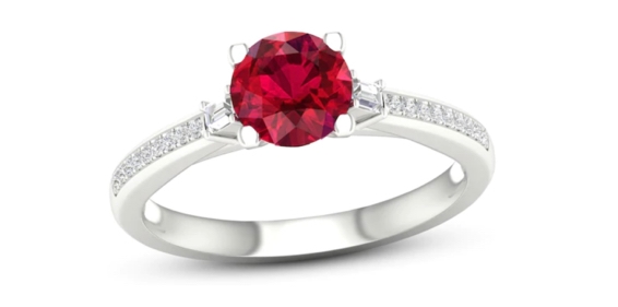 White gold engagement ring with round red gemstone center stone and round diamond side stones.